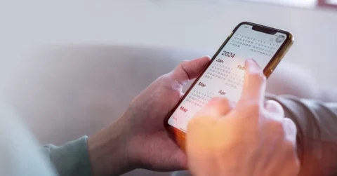Das Bild zeigt ein Handy, welches von zwei Händen gehalten wird und einen Terminkalender zeigt.