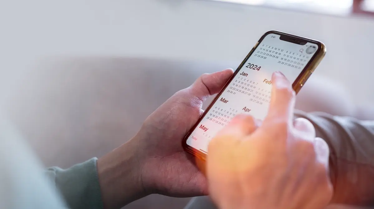 Das Bild zeigt ein Handy, welches von zwei Händen gehalten wird und einen Terminkalender zeigt.