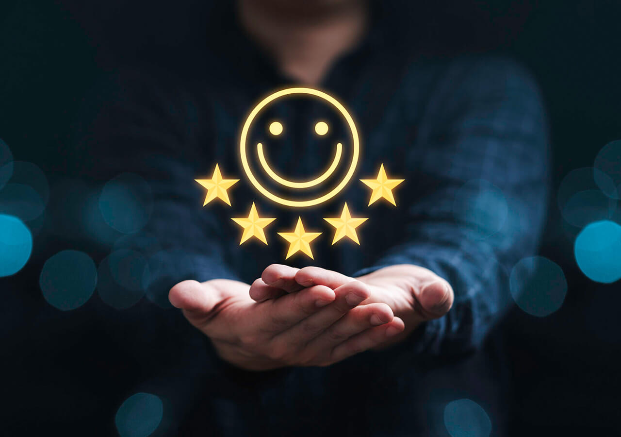 Eine Person hält ihre Hände mit einem leuchtenden gelben Smiley-Gesicht und fünf darüber schwebenden Sternen, die hohe Zufriedenheit mit einer innovativen Cloud Contact Center Lösung symbolisieren. Der Hintergrund ist dunkel und unscharf.